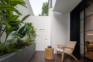 Un espacio exterior moderno con terraza de madera, silla de mimbre y plantas en macetas.