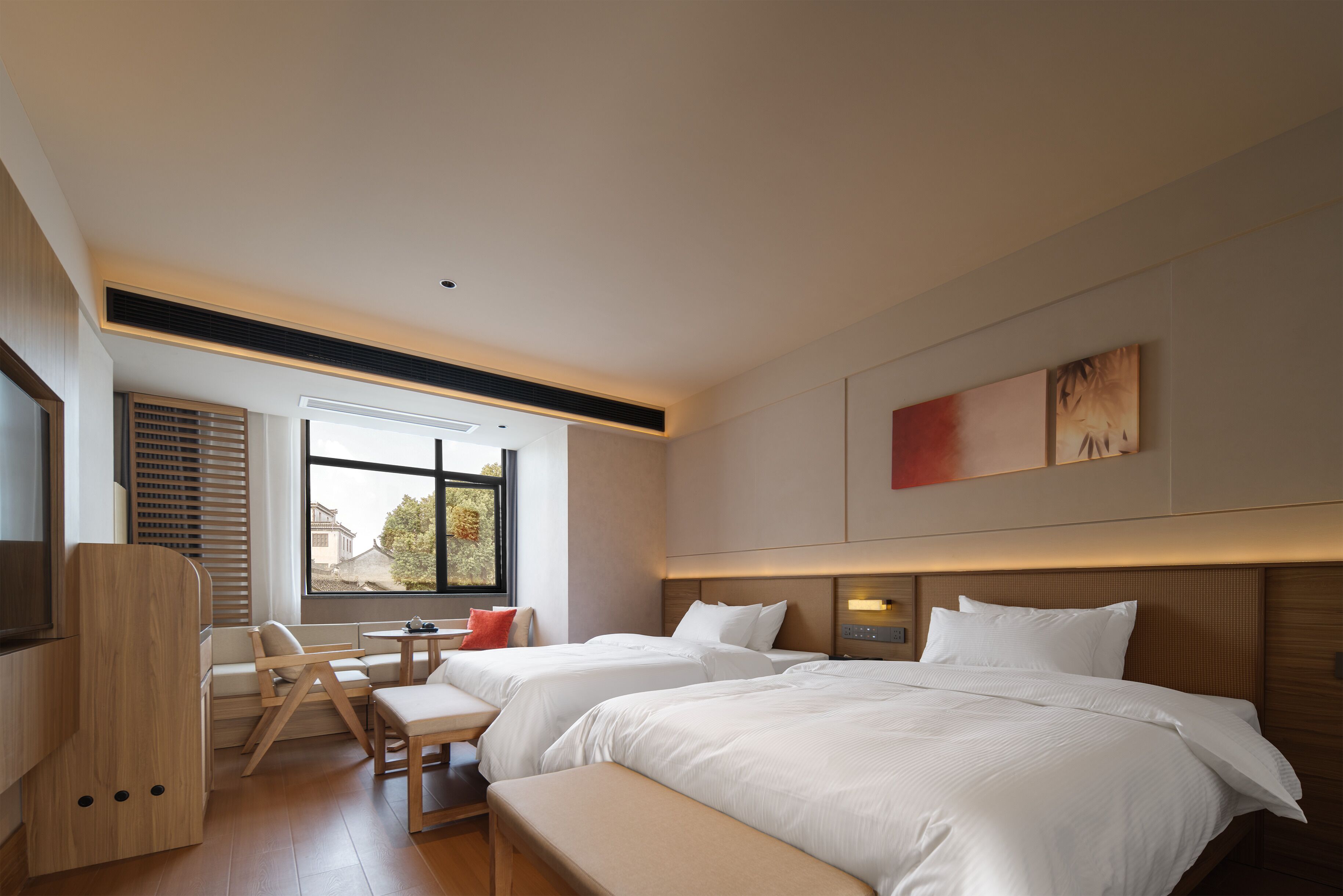 A modern hotel room with two beds, a seating area, and a large window.