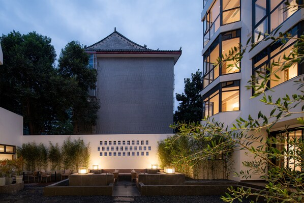 A courtyard with a traditional building, seating area, and modern building with illuminated windows. - Maiyue Hotel (Xi'an)