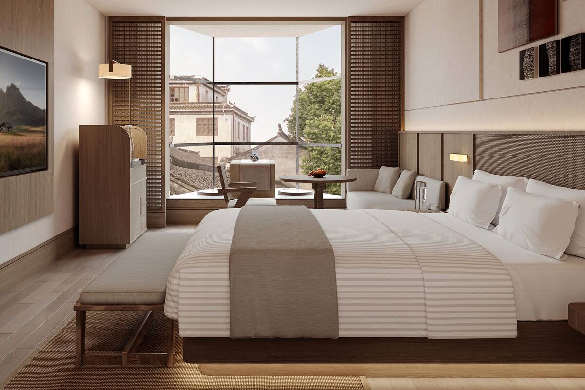 Habitación de hotel moderna con una cama grande, un área de descanso con mesa y vistas a la arquitectura tradicional a través de amplias ventanas.