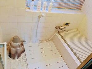 Kylpyhuone, jossa on kylpyamme, suihkupää ja hylly, jossa on hygieniatuotteita.