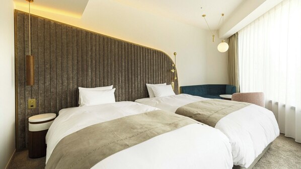 Ein Hotelzimmer mit zwei Betten, einem blauen Sofa, einem runden Tisch und einer modernen Leuchte.