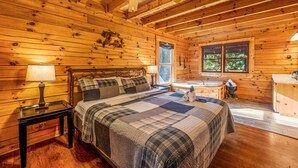 A wooden cabin bedroom with a bed, nightstands, a window, and a bathroom with a bathtub.