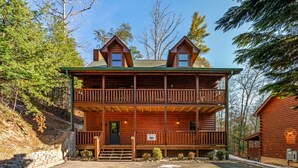 A two-story log cabin with a balcony, surrounded by trees.