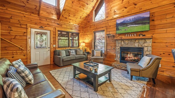 A cozy log cabin interior with a fireplace, a sofa, a coffee table, and a television mounted on the wall.