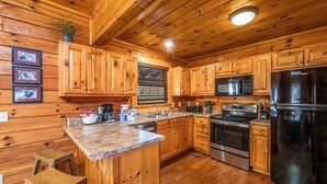 A wooden cabin-style kitchen with granite countertops, wooden cabinets, a stainless steel refrigerator, and a built-in microwave.