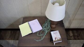 Ein kleiner Holztisch mit einem Spiralheft, einer Zierpflanze, einem Buch mit dem Titel 'KJV Devotional' und einer weißen Tischlampe.
