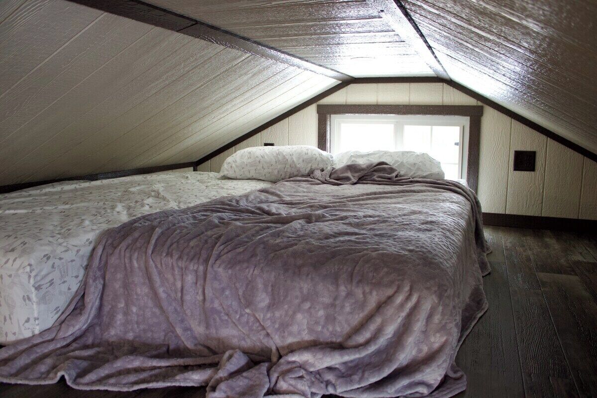Un dormitorio en el ático con techo inclinado, una cama con colcha estampada y un ventanal.