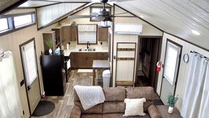 Een compact camperinterieur met een kitchenette, een bank met kussens, een plafondventilator en een kleine tafel met een plant.
