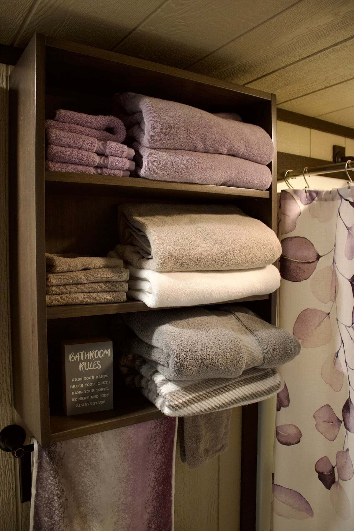 A shelf with neatly folded towels in shades of purple and beige.