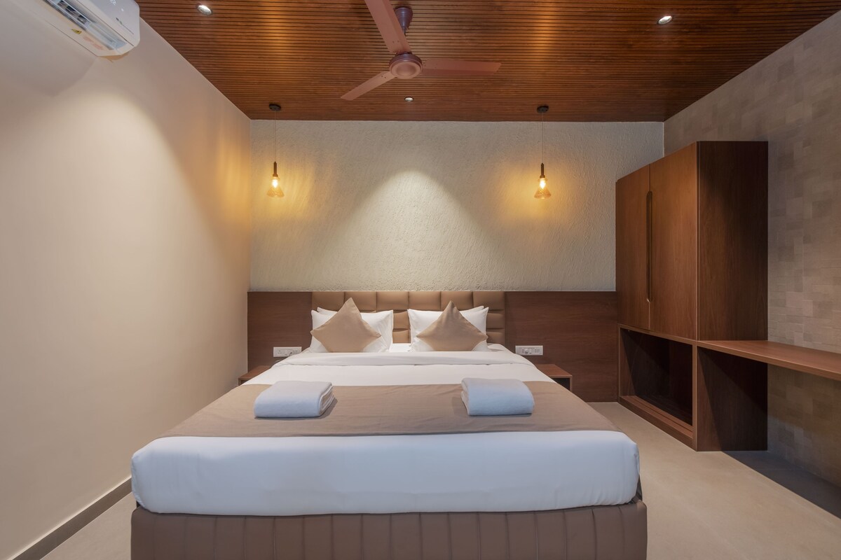 A modern hotel room with a large bed, wooden ceiling, two pendant lights, and a built-in wardrobe.