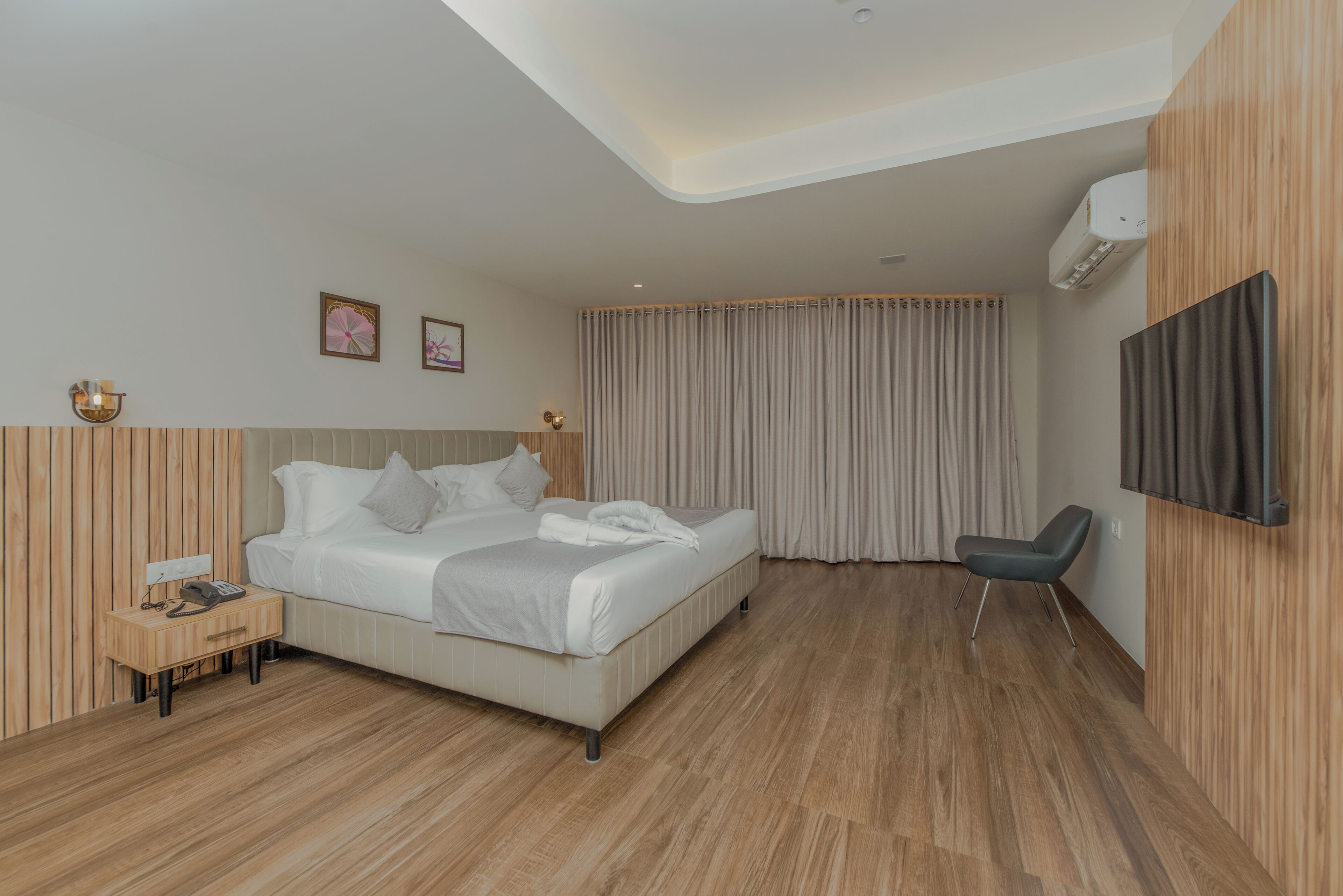 A modern hotel room with a bed, bedside table, chair, and a large window with curtains.