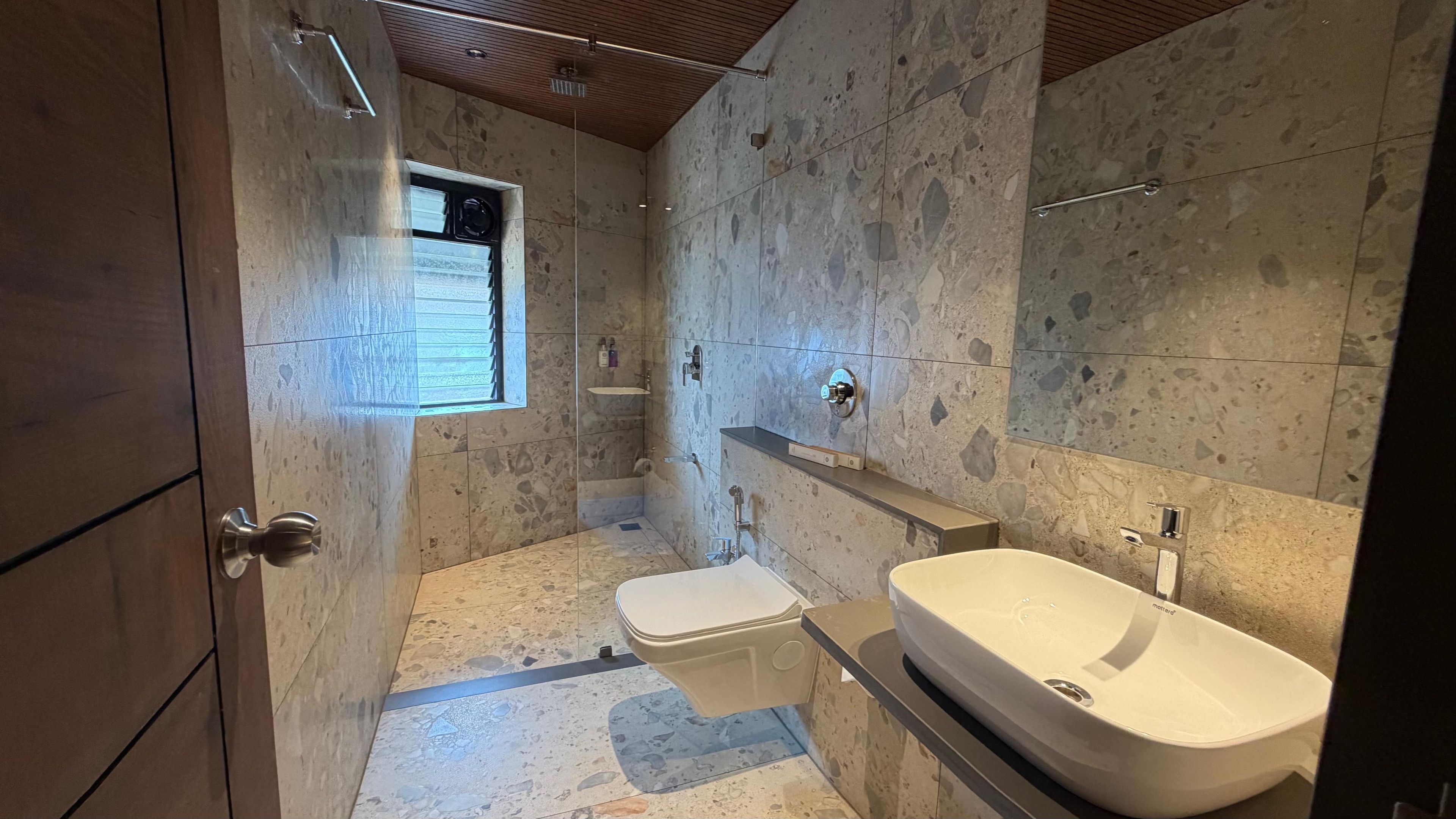 A bathroom with a stone wall, a window, a toilet, and a sink.