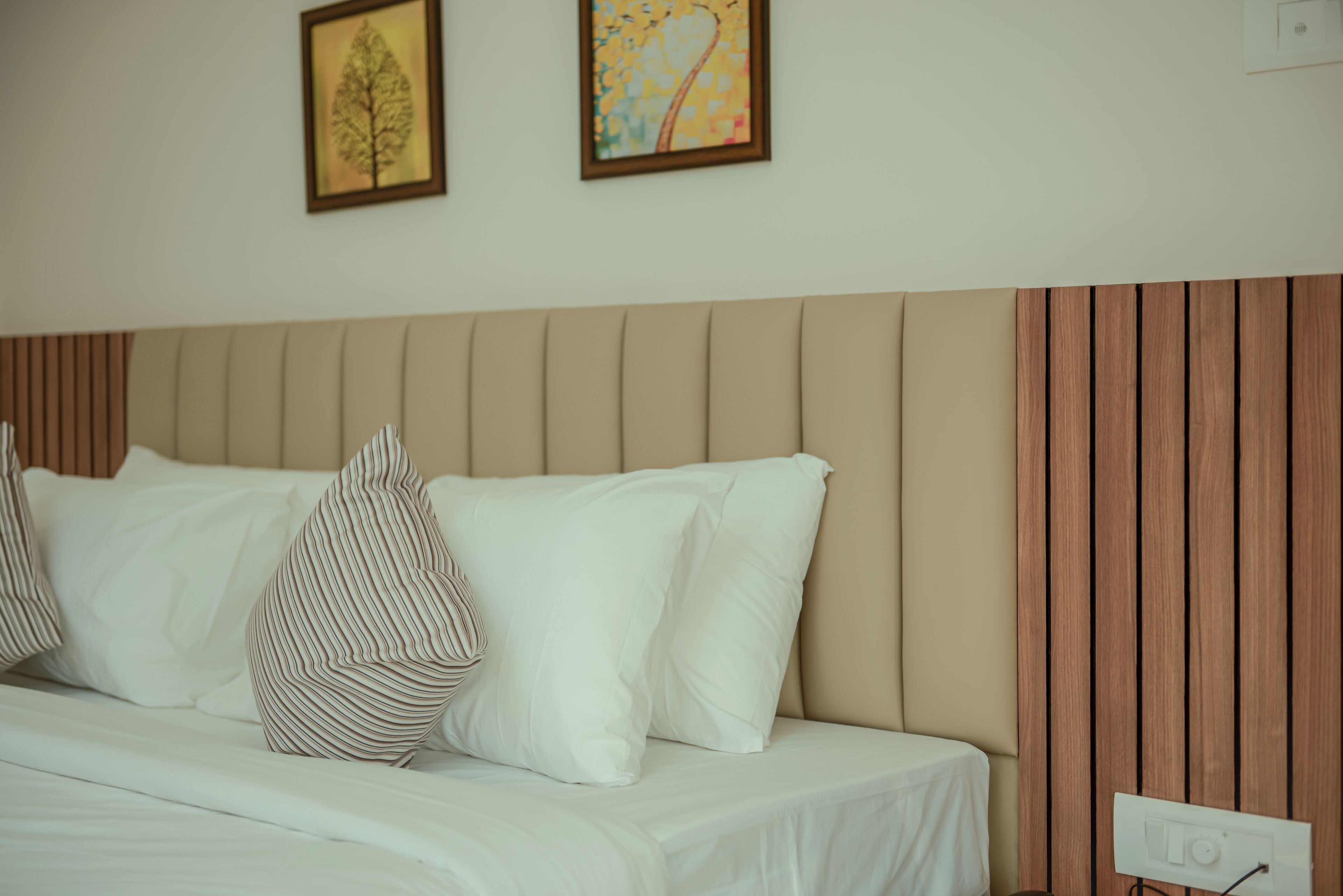 Una cama bien hecha con ropa de cama blanca y almohadas a rayas, un cabecero de madera y dos cuadros enmarcados en la pared.