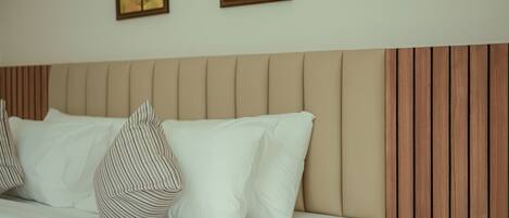 A neatly made bed with white bedding and striped pillows, a wooden headboard, and two framed artworks on the wall.