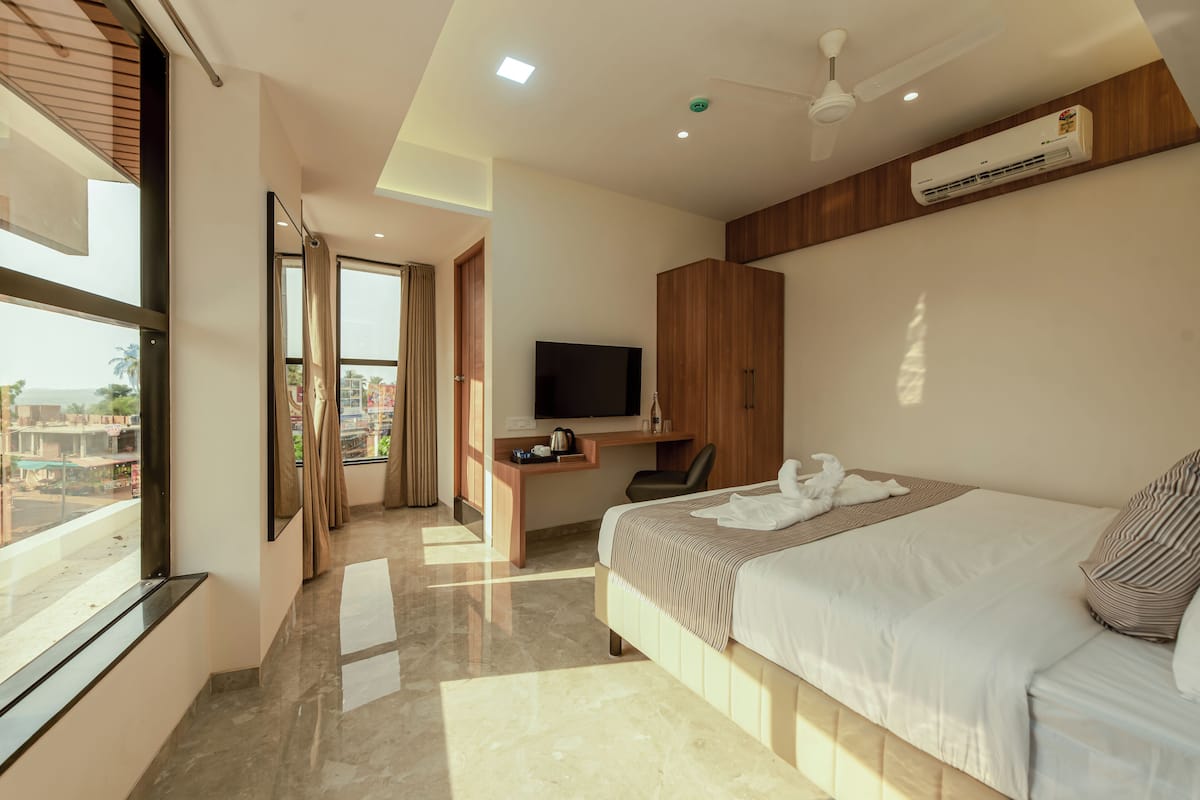 A modern hotel room with a large bed, a desk with a TV, and a view of the city.