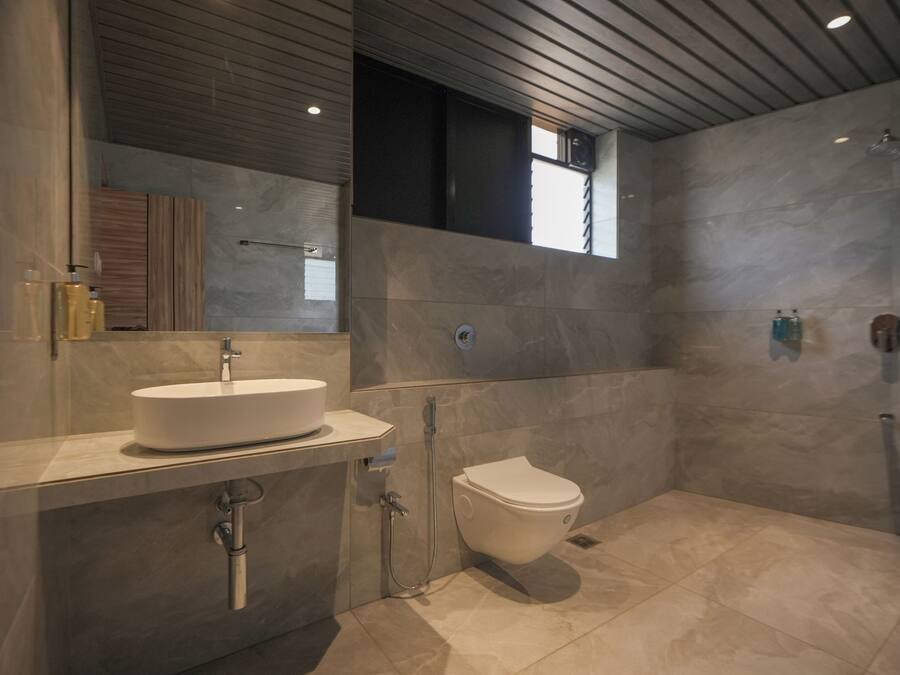 A modern bathroom with a large mirror, a white sink, a toilet, and a shower area.