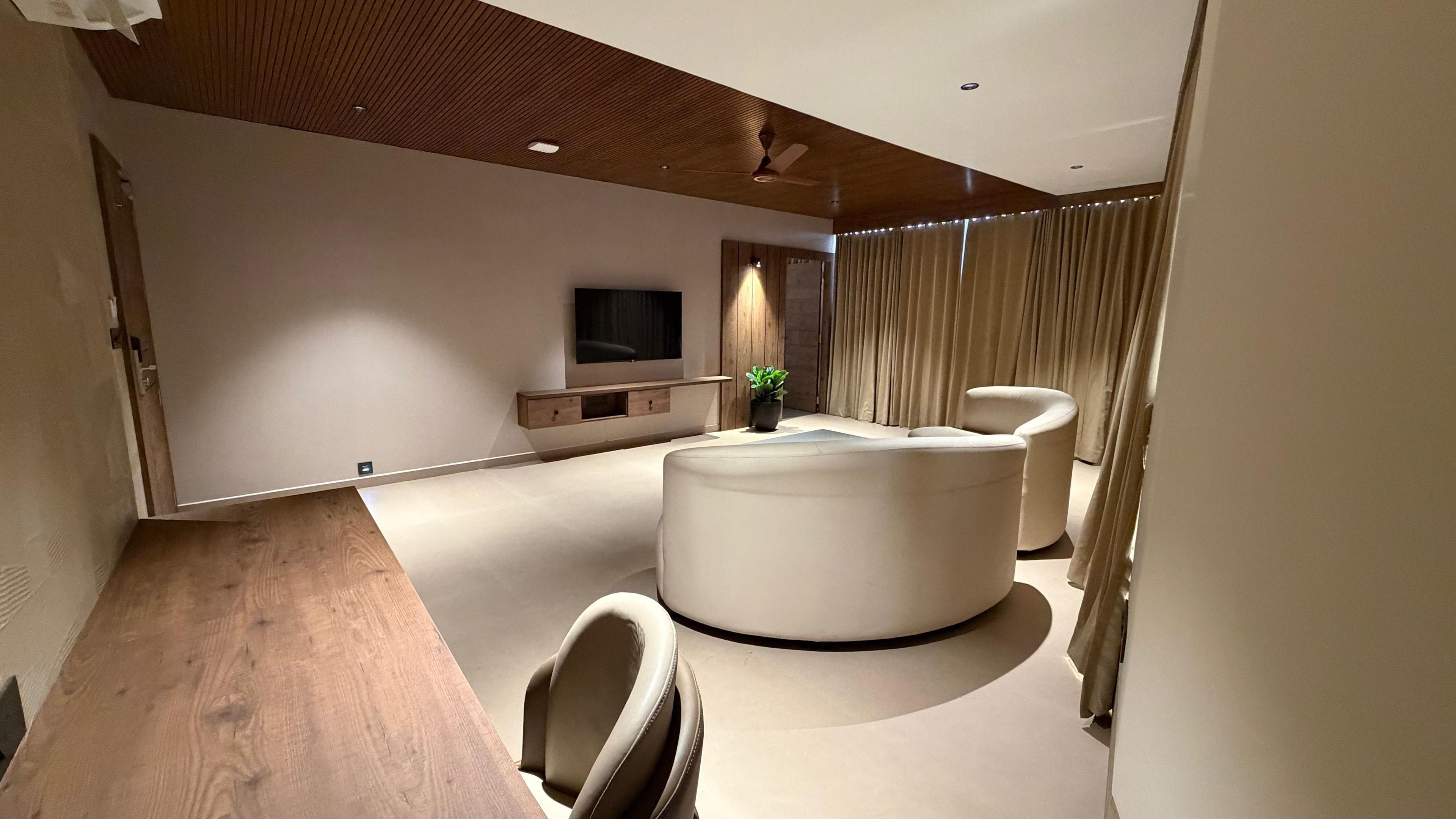 Una sala de estar moderna con techo de madera, un televisor de pantalla plana, un sofá, un sillón y una planta en maceta.