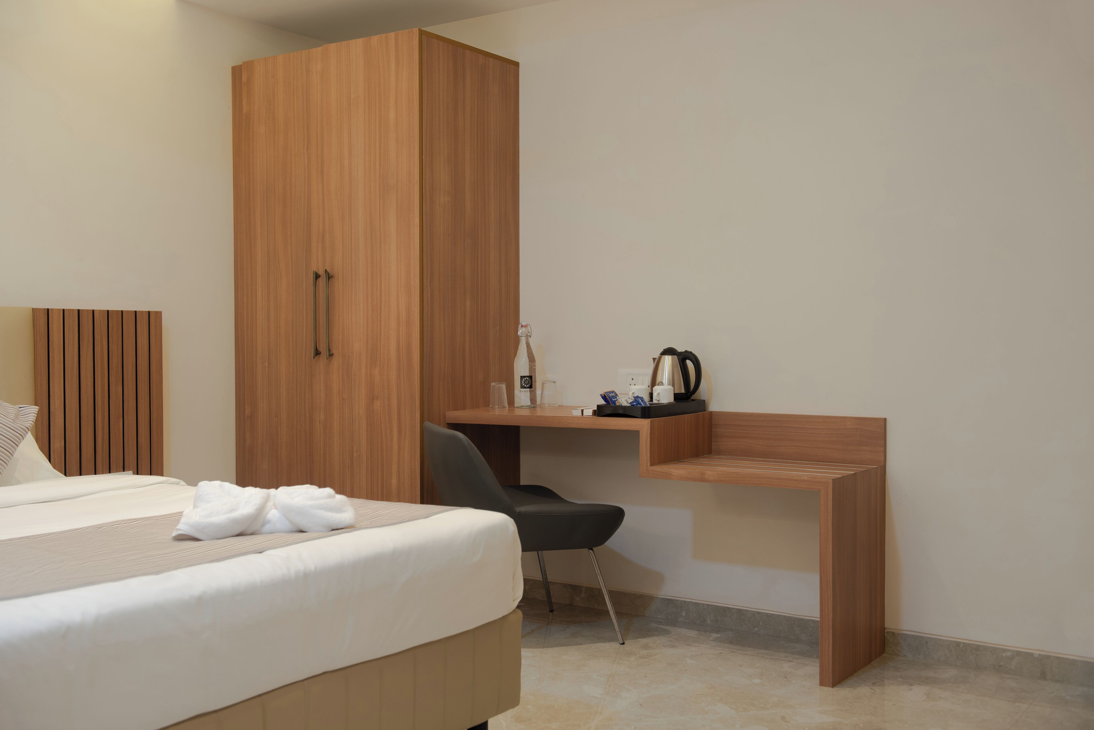Una habitación de hotel con cama, un armario de madera, un escritorio con silla y una tetera sobre el escritorio.
