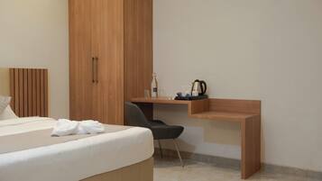 Una habitación de hotel con cama, un armario de madera, un escritorio con silla y una tetera sobre el escritorio.