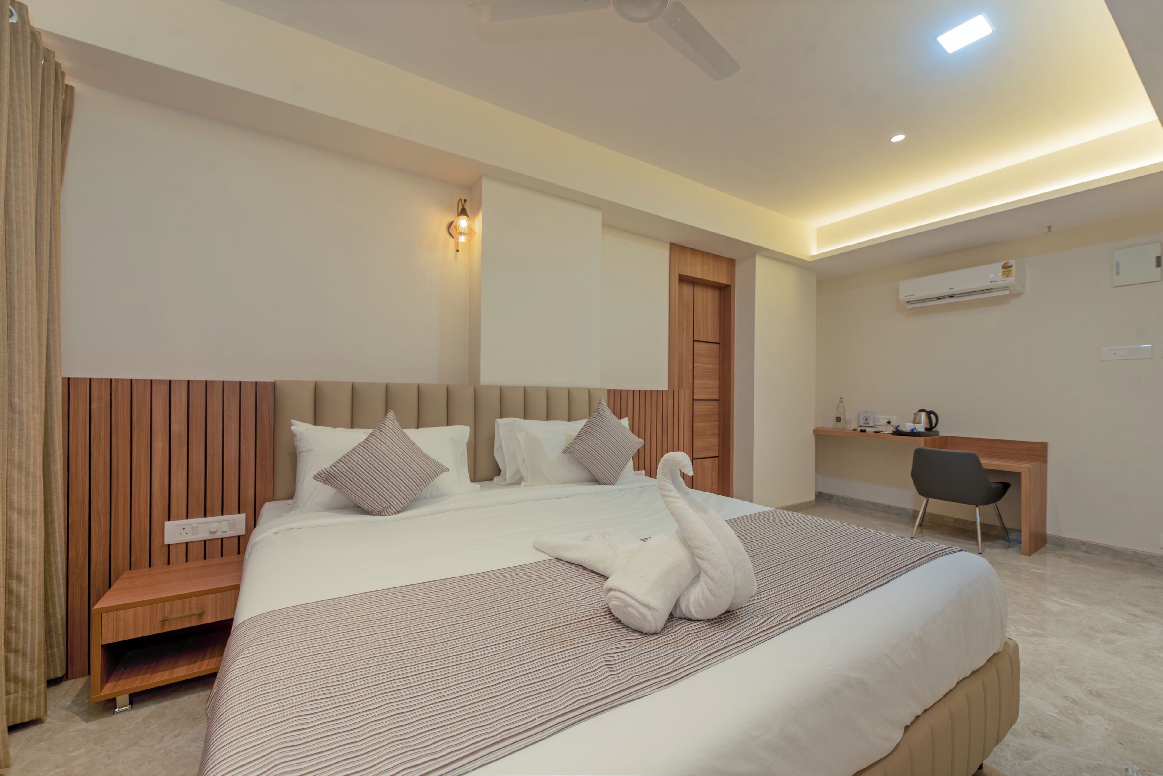 A modern hotel room with a large bed, a wooden headboard, a desk, and a chair.
