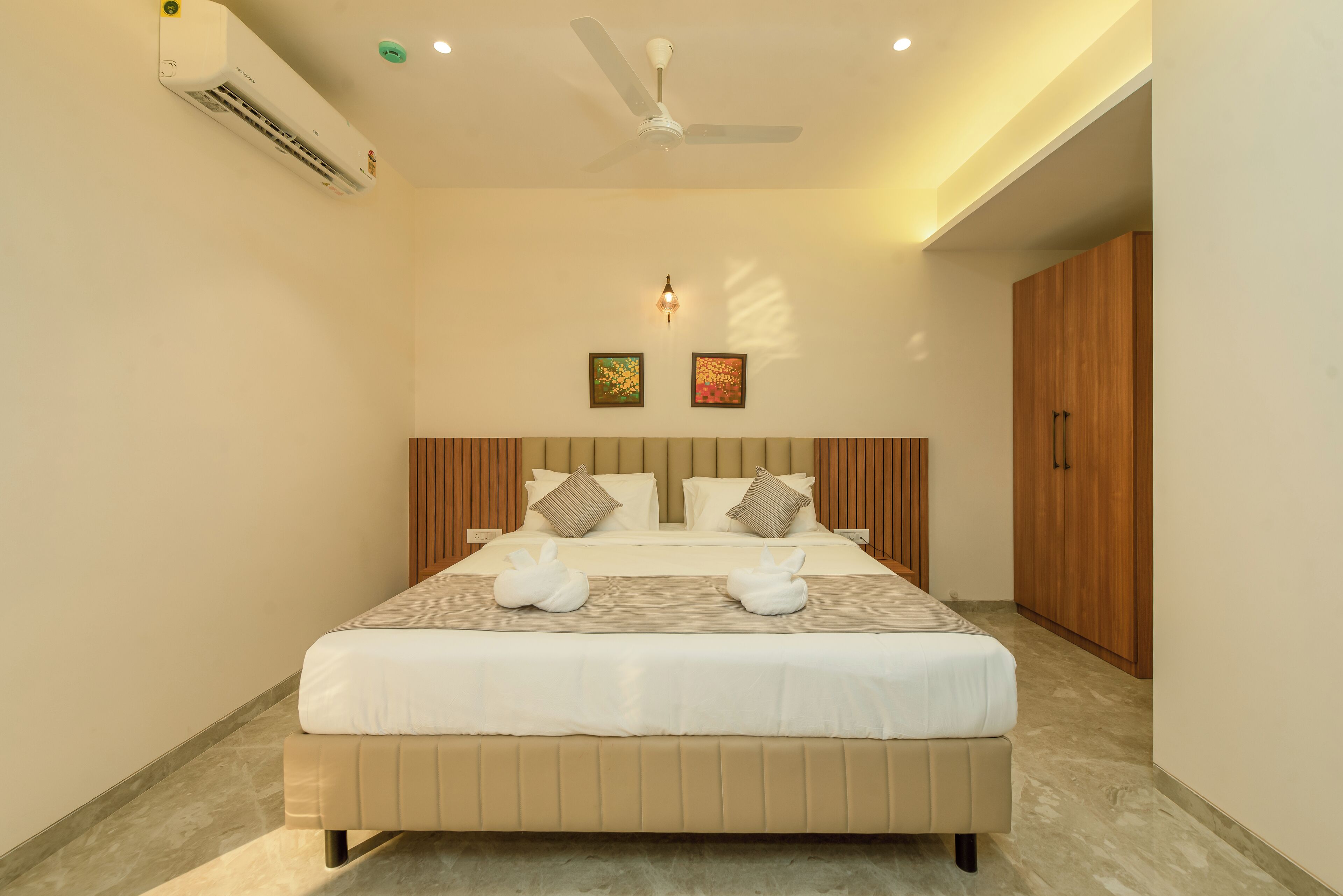 A neatly arranged hotel room with a large bed, a ceiling fan, an air conditioning unit, and wooden wardrobes.