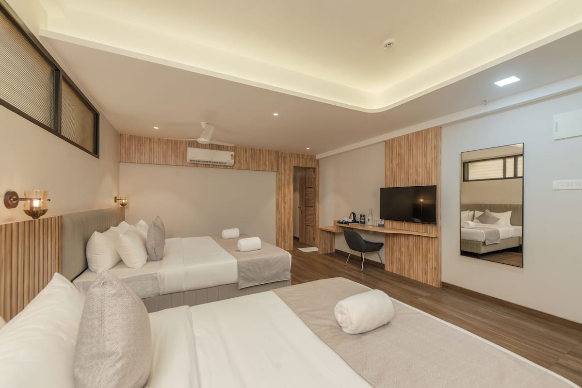 A modern hotel room with two beds, a desk, a TV, and a mirror.