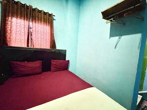 Ein kleines Zimmer mit einem Einzelbett, einem hölzernen Kopfteil, zwei Kissen und einer roten Bettdecke.