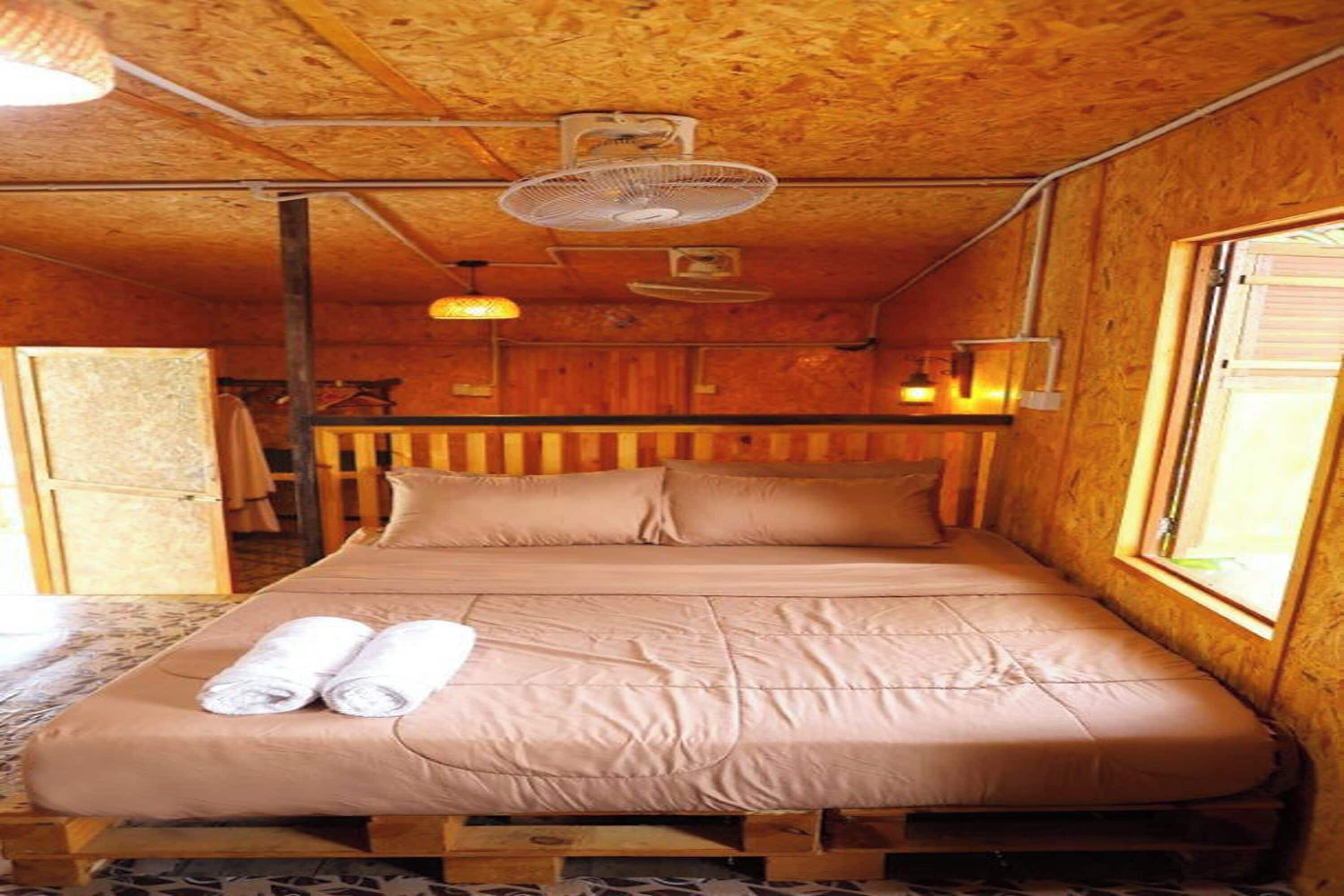 Una habitación de cabaña de madera con una cama, dos ventiladores y una ventana.