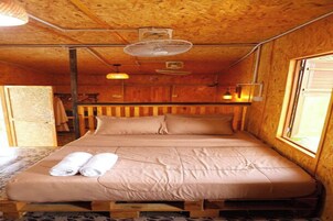 Una habitación de cabaña de madera con una cama, dos ventiladores y una ventana.