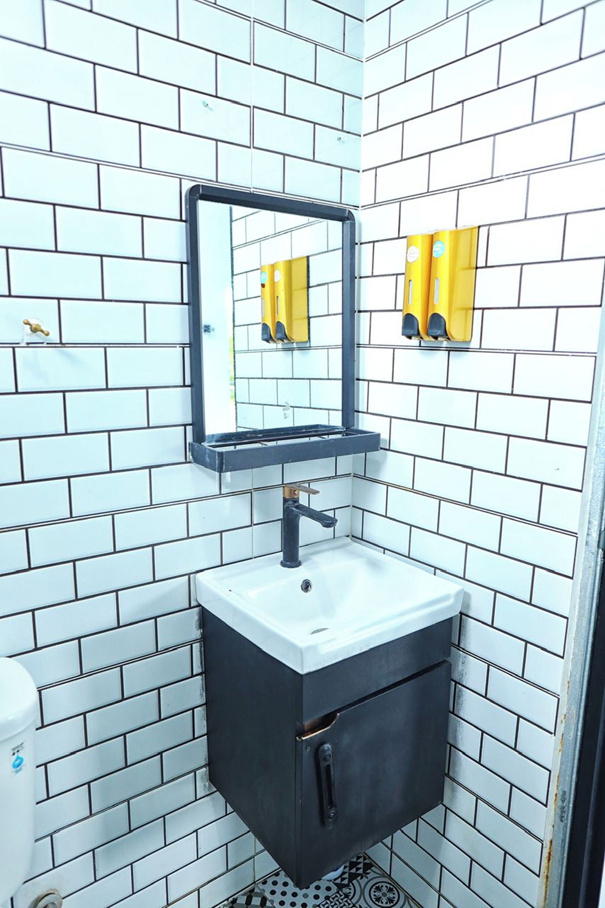 Un baño con paredes de azulejos blancos y negros, un lavamanos blanco con gabinete negro y un espejo sobre el lavamanos.