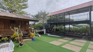Un patio con césped artificial, una estructura de madera y una zona cubierta con plantas.