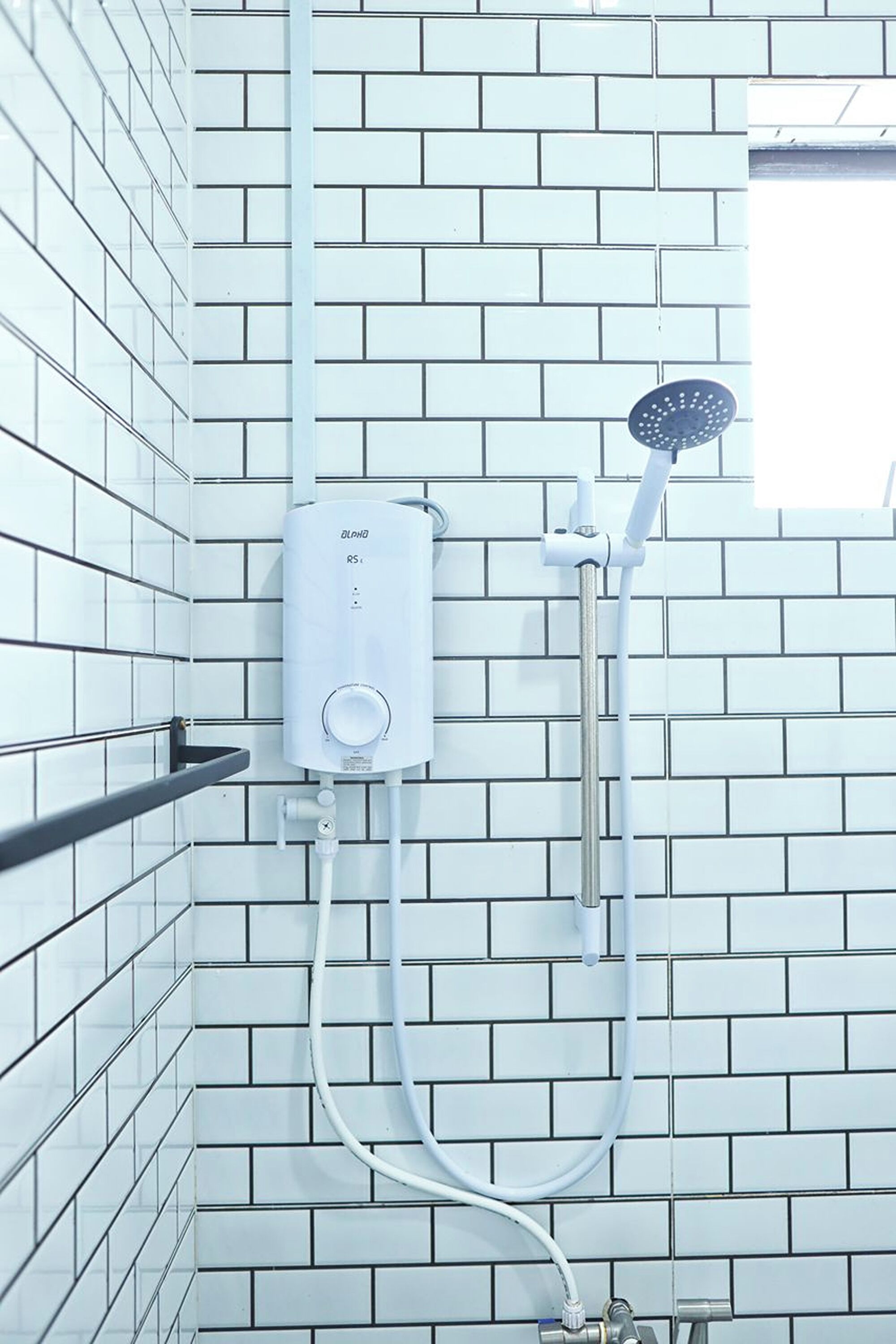 Un baño con paredes de azulejos blancos, una cabina de ducha blanca y una barandilla de metal.
