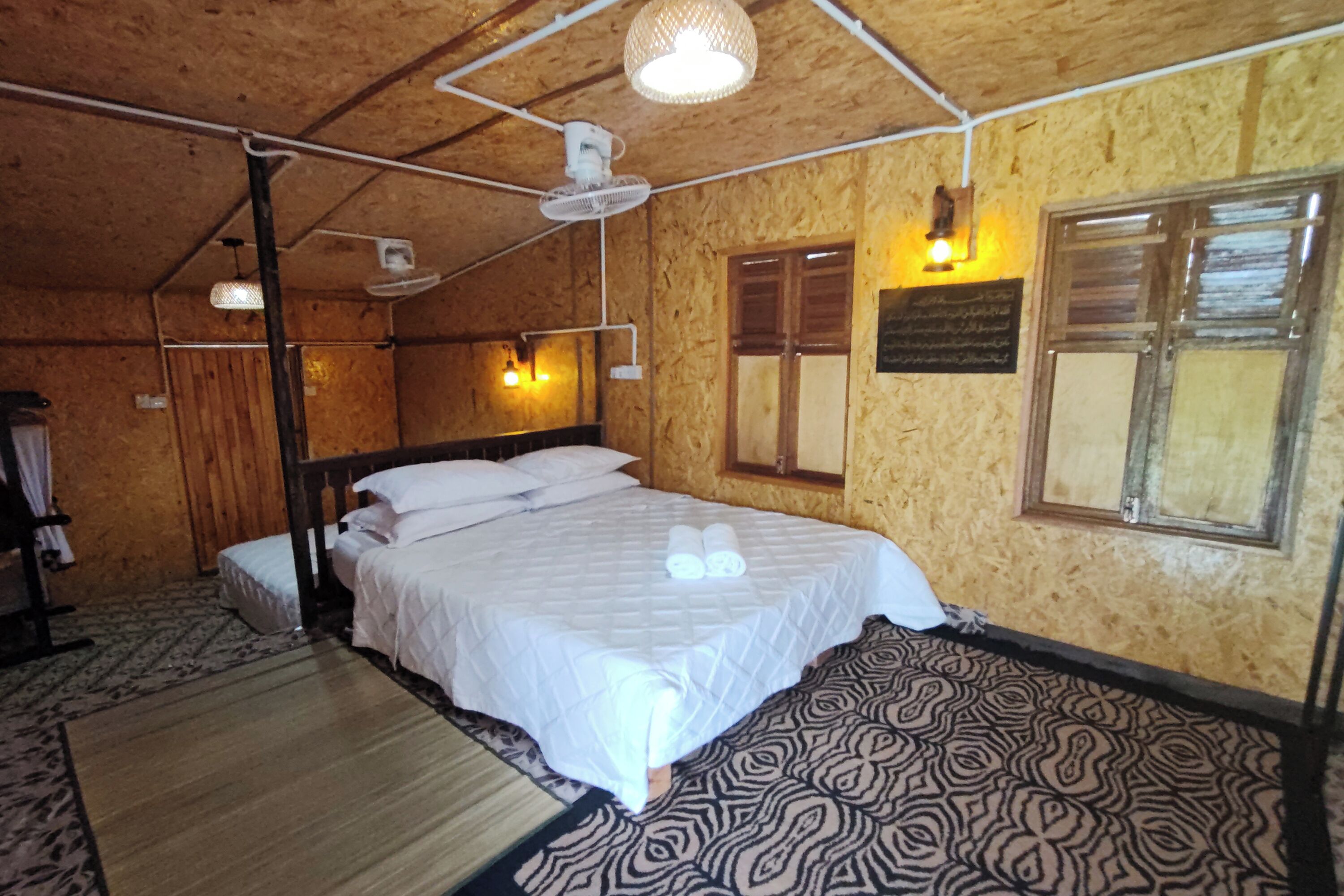 Una habitación con una cama, una ventana y una lámpara fijada a la pared.