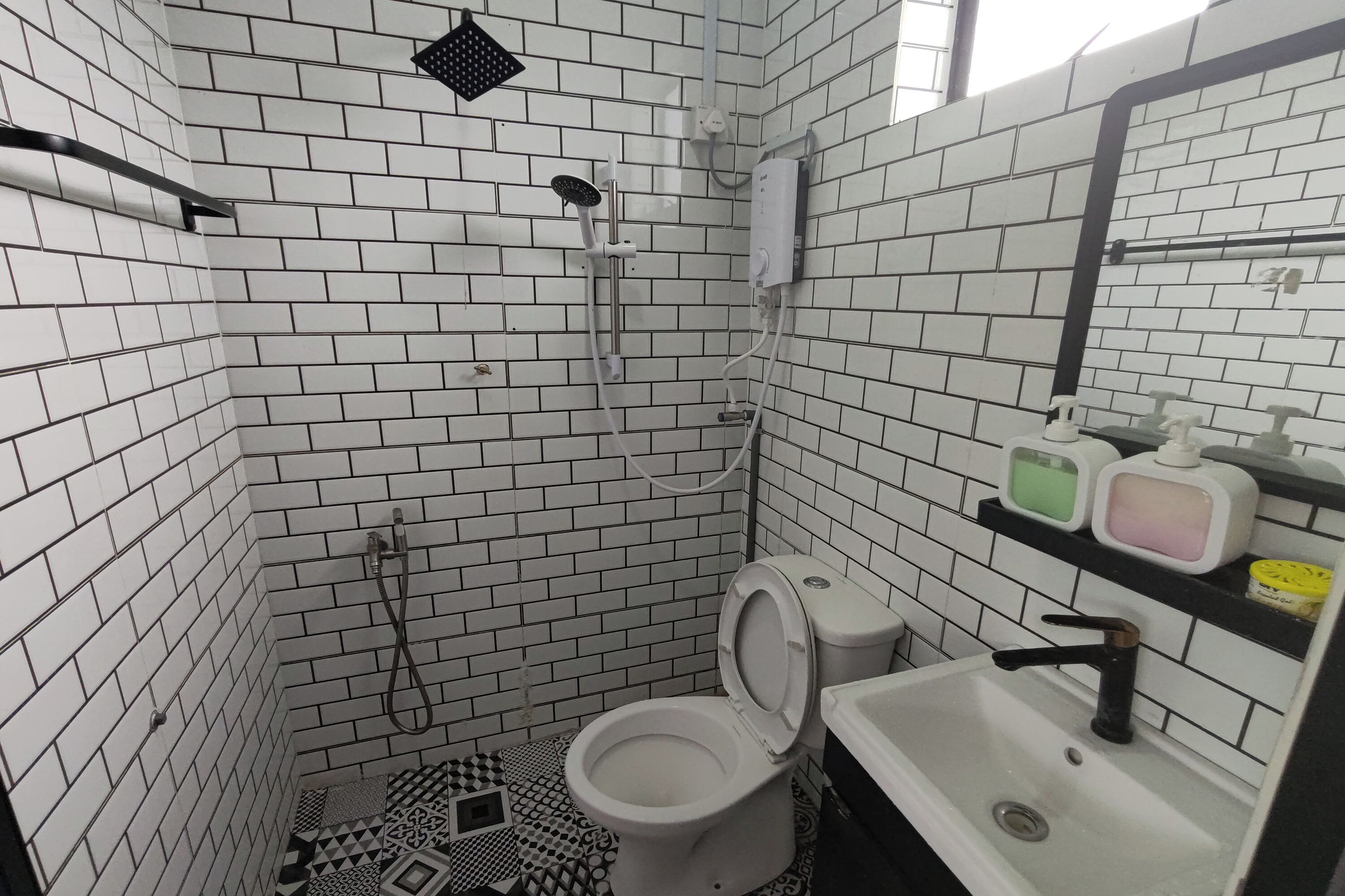 Een badkamer met witte betegelde wanden, een douche, toilet en een wastafel met zeepdispensers.