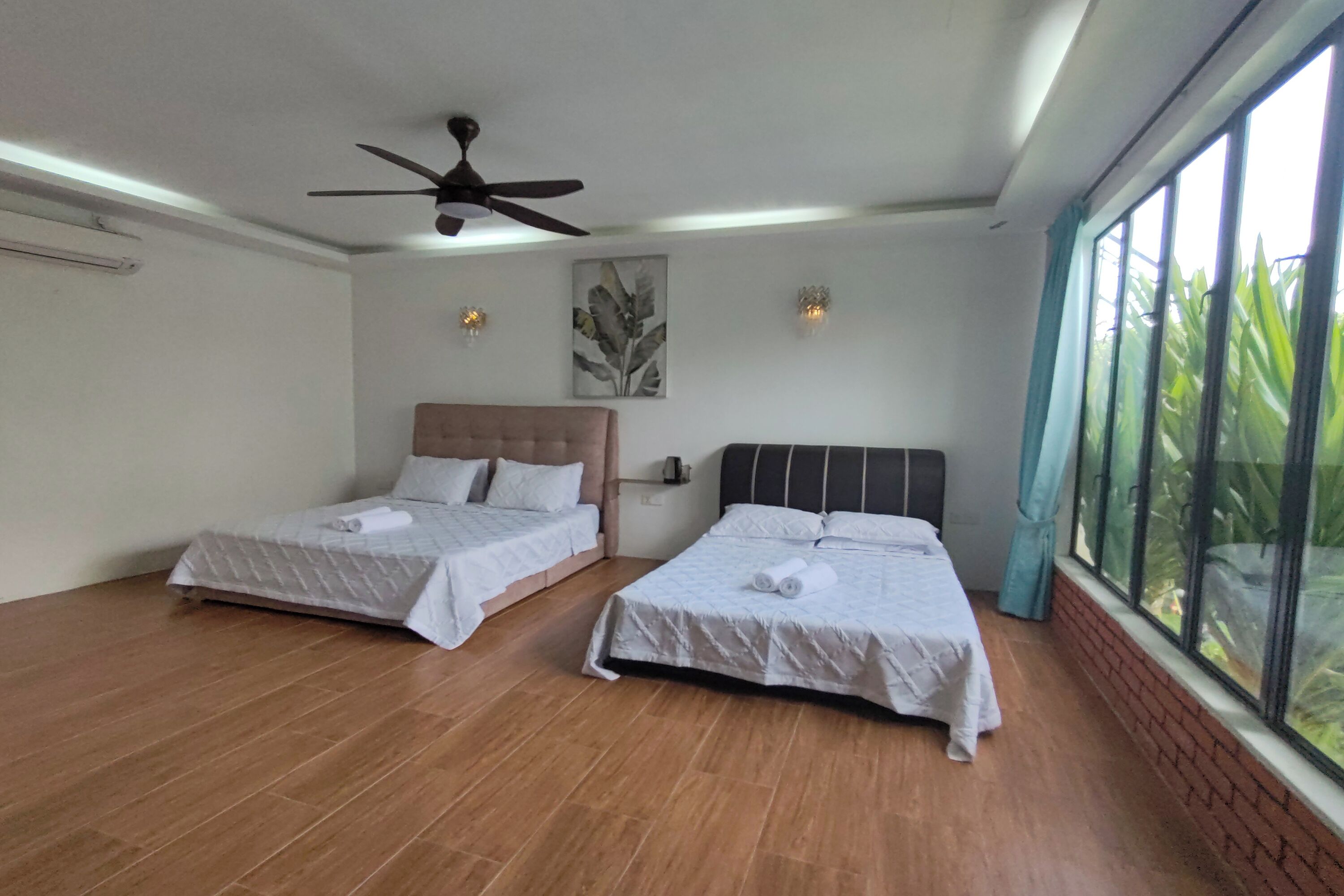 A bedroom with two beds, a ceiling fan, and a large window with a view of greenery.
