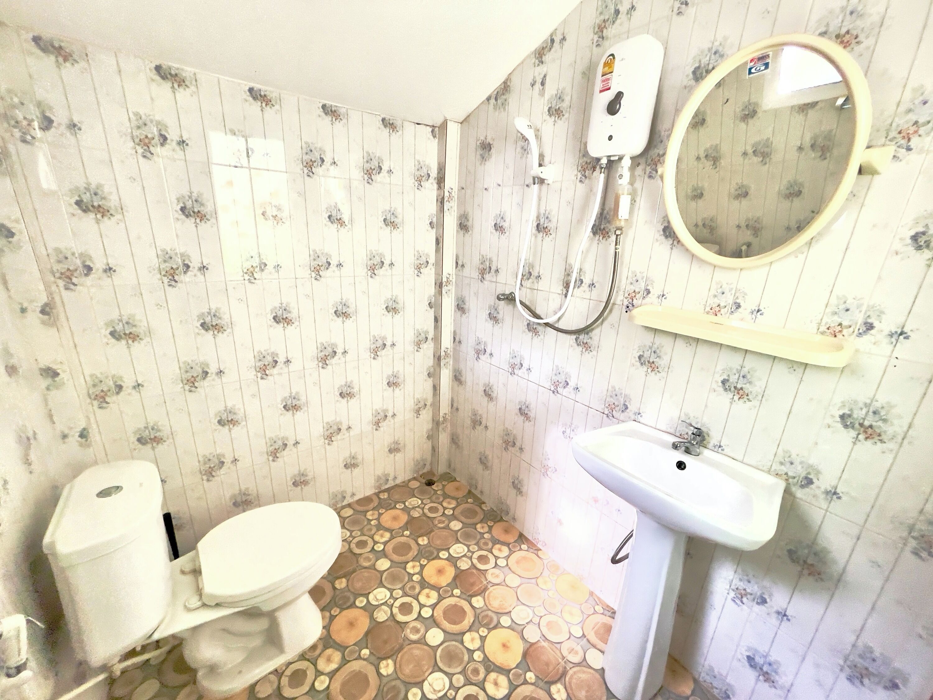 Ein Badezimmer mit Toilette, Waschbecken, Dusche und Wandgestaltung mit floralem Muster.