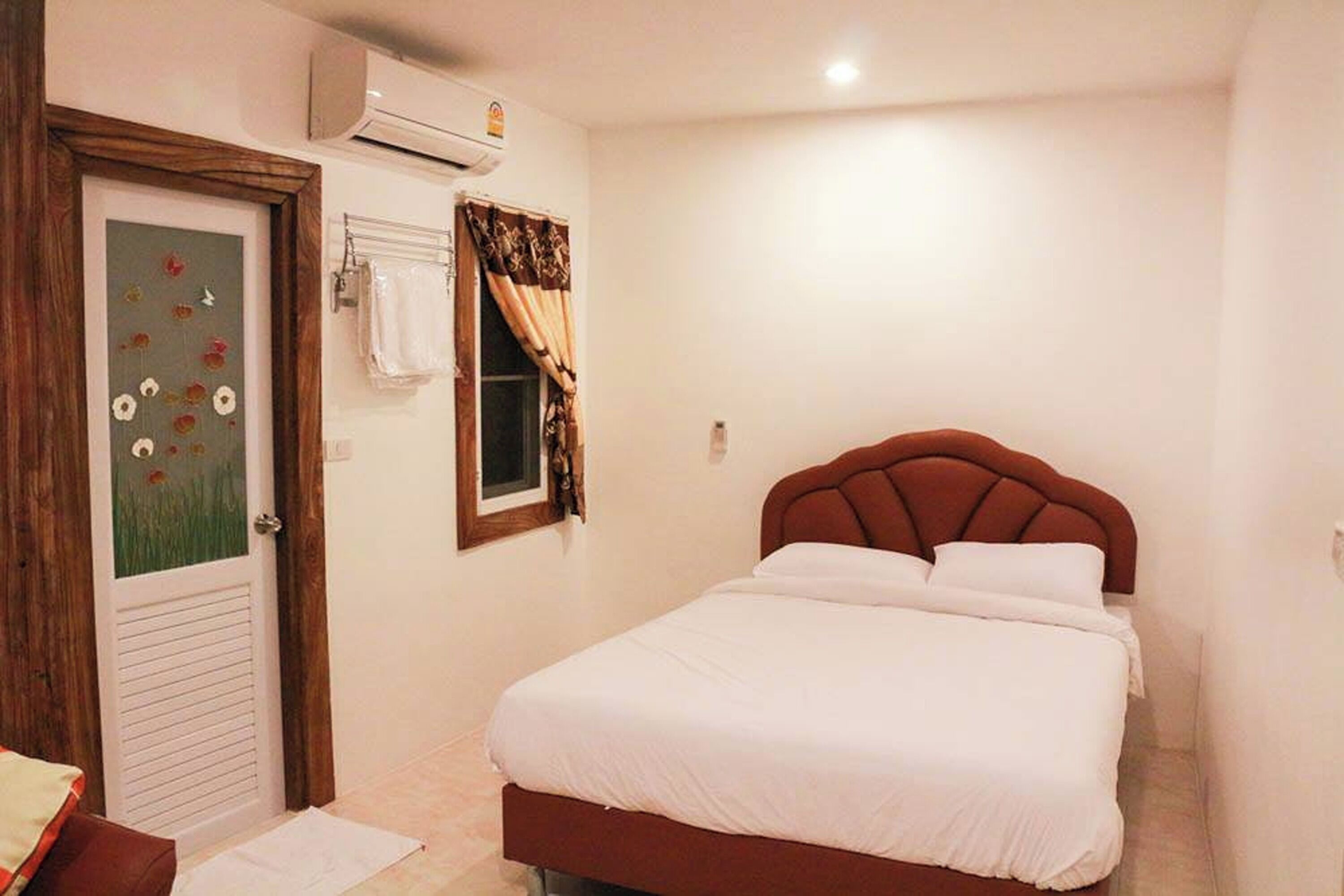 Un dormitorio con cama, ventana con cortinas, puerta con panel de vidrio satinado y un equipo de aire acondicionado en la pared.