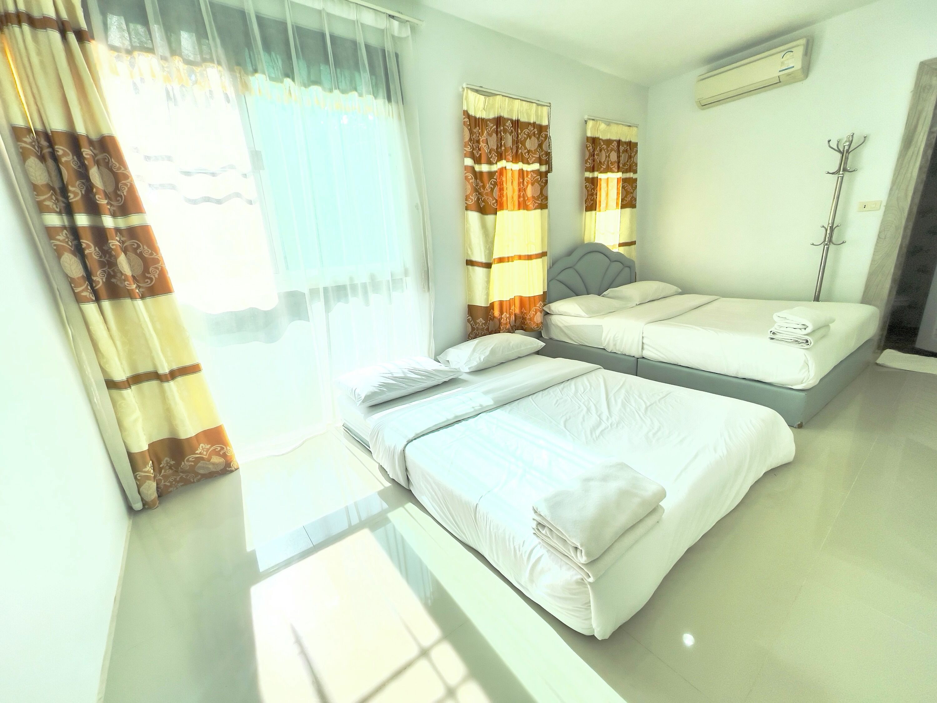 A hotel room with two beds, a large window with curtains, a bedside table, and a wall-mounted air conditioner.
