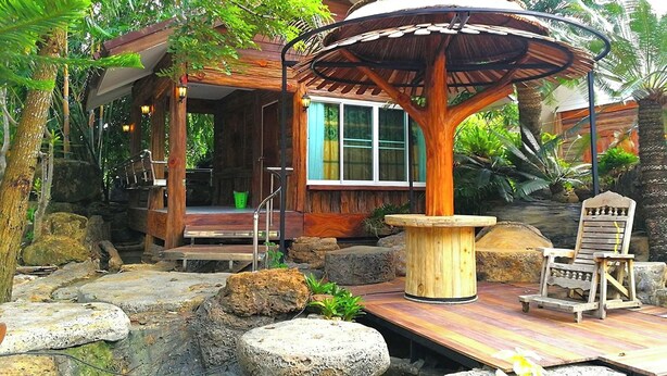 Une structure en bois dotée d’un espace de repos abrité, entourée de rochers et de plantes.
