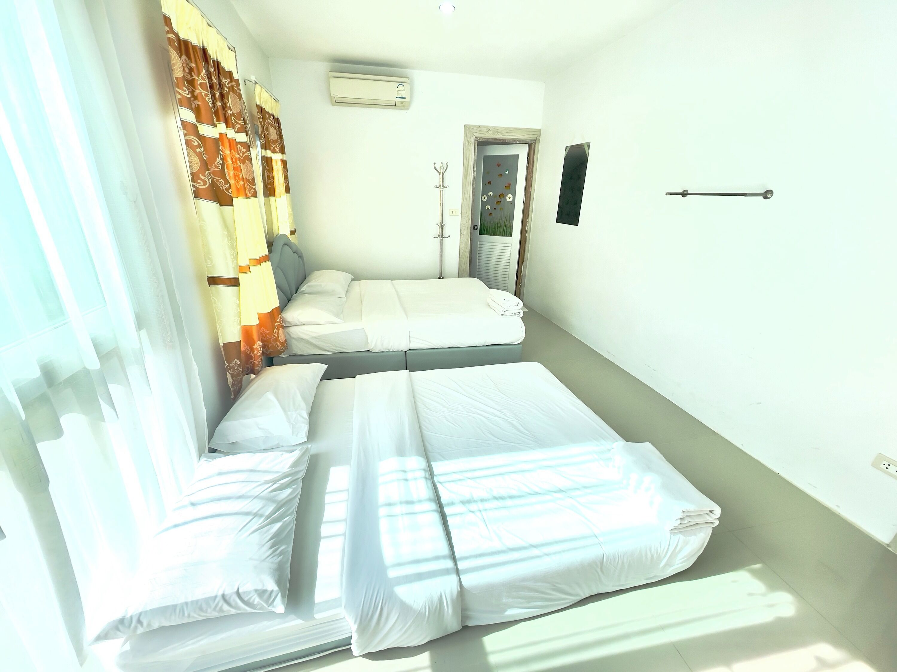 A room with two beds, a door, an air conditioning unit, and a wall-mounted hook.
