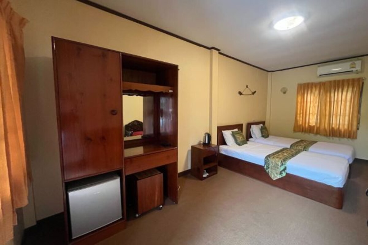 A hotel room with a bed, a desk, a small refrigerator, a wardrobe, and a bedside table.