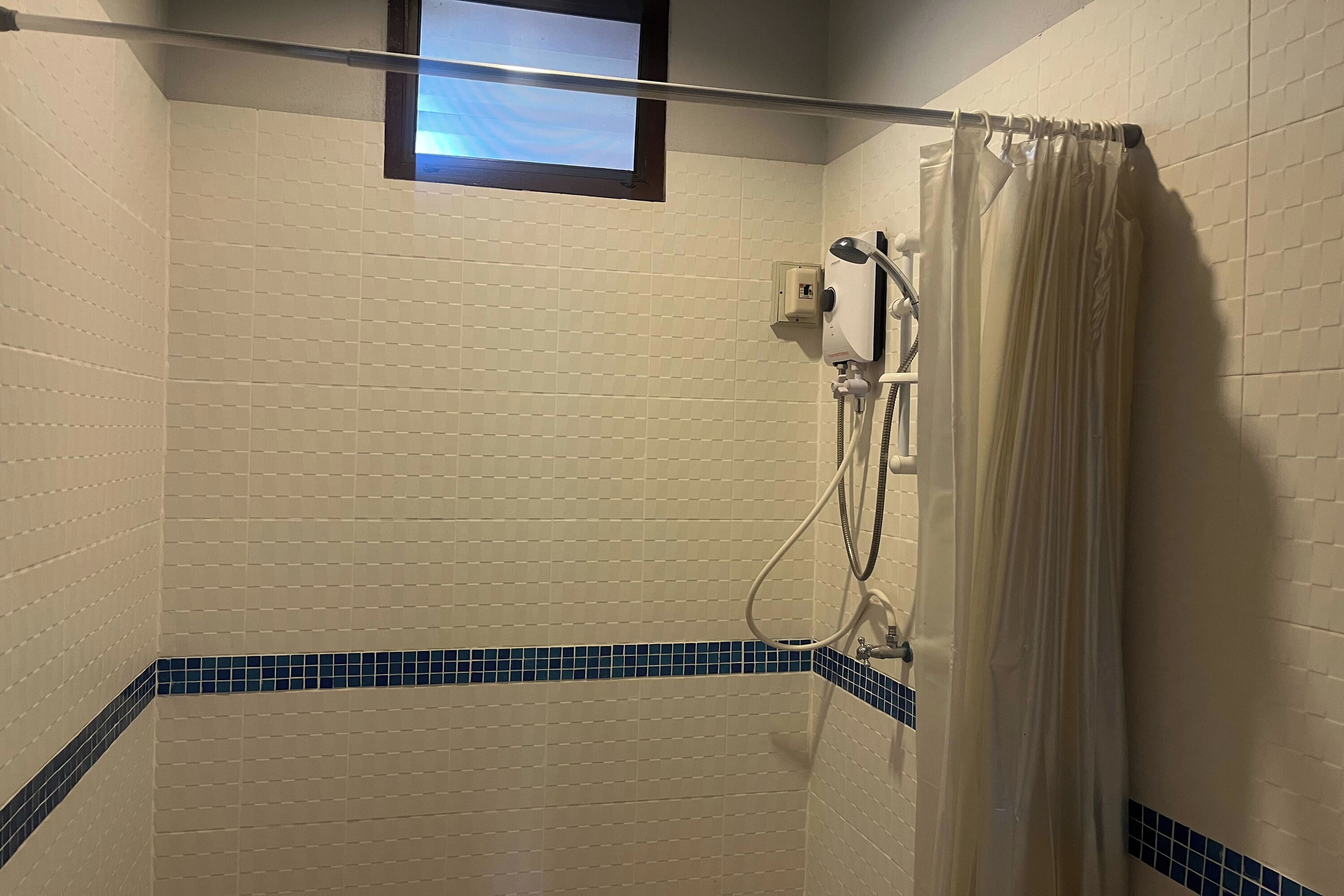 Ducha con cortina, ventana y un borde de azulejos azules.