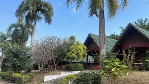 A building with a green roof and a red facade, surrounded by palm trees and various shrubs. - Pai Hillside Resort (Pai)
