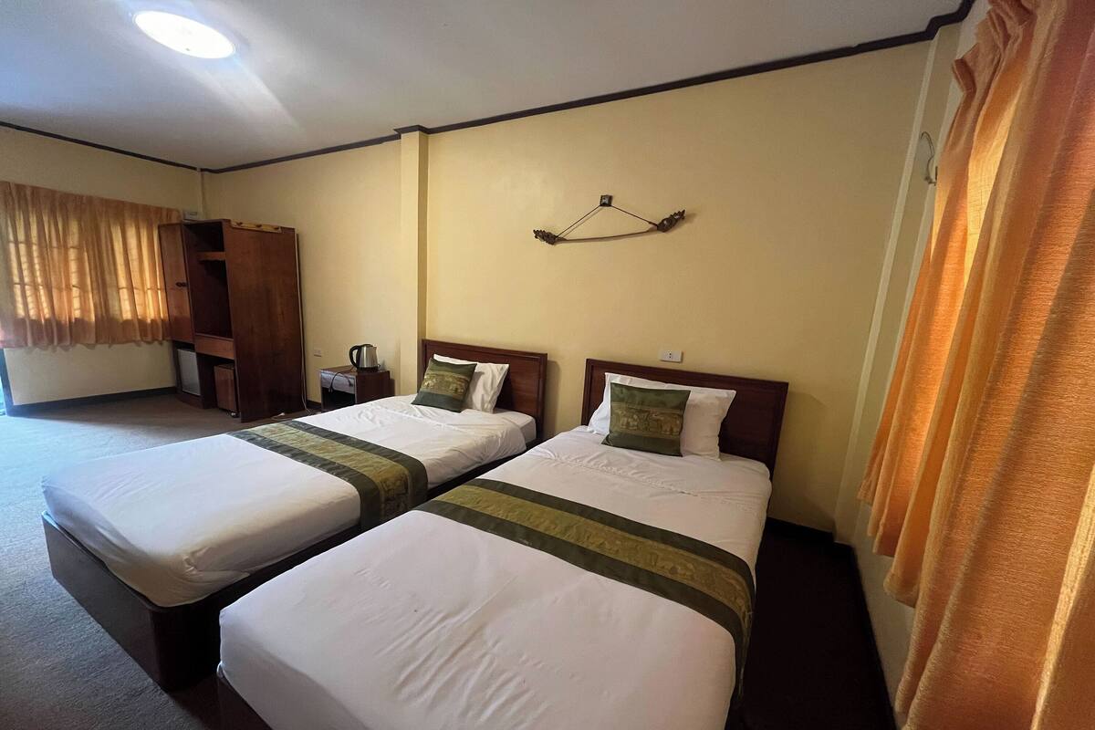 A hotel room with two single beds, a wardrobe, a small table, and a hanging light fixture.