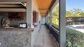 A covered outdoor area with a counter displaying merchandise, a QR code, and a brick wall with a logo. - Namkhem Inn (Takua Pa)