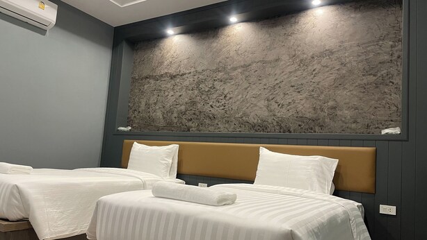 A hotel room with two beds, a large textured wall art piece above the beds, and a ceiling light fixture. - Namkhem Inn 2 (Takua Pa)