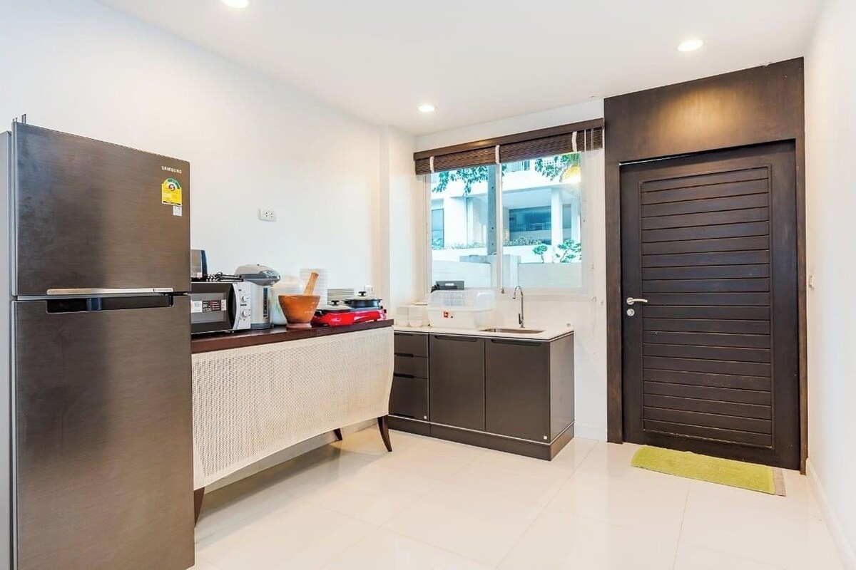 A compact kitchen with a stainless steel refrigerator, a microwave, a sink, and a window with a view of greenery outside.