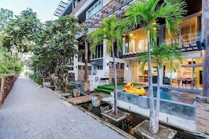 Un hotel moderno con piscina, mobiliario exterior y un callejón estrecho.