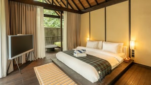 A hotel room with a bed, a TV, and a view of greenery outside. - Rumah Lituhayu (Tabanan)